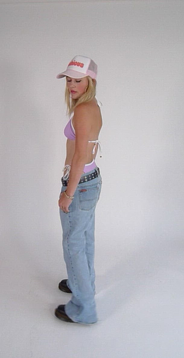 Girl wearing baby pink bikini with baggy blue jeans and a logo trucker hat.